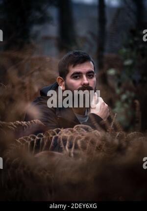Beautiful portrait of young man with black beard and black hair looking at the camera surrounded by beautiful plants with an orange tone due to autumn
