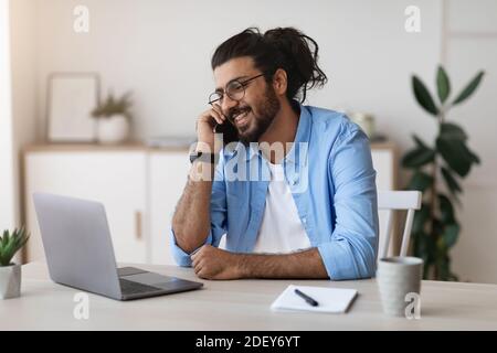 Western Freelancer Guy Talking On Cellphone And Working On Laptop At Home Stock Photo
