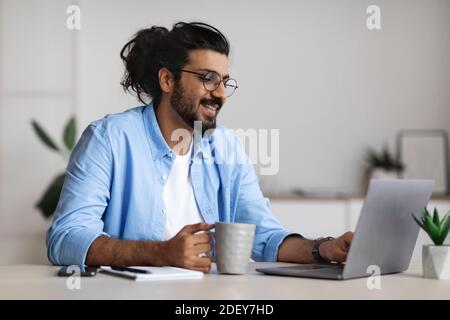 Pros of Freelancing. Positive Freelancer Guy Drinking Coffee And Working On Laptop Stock Photo