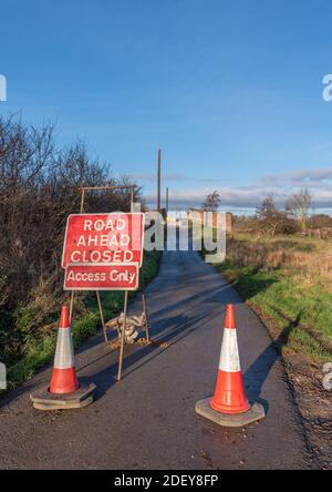 Road ahead closed sign and 2 red and white traffic cones on approach to a closed bridge. Stock Photo