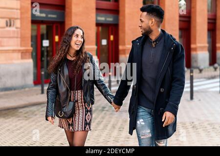 Stock photo of happy moment of interracial couple holding hands and looking at each other. They are in Madrid city Stock Photo