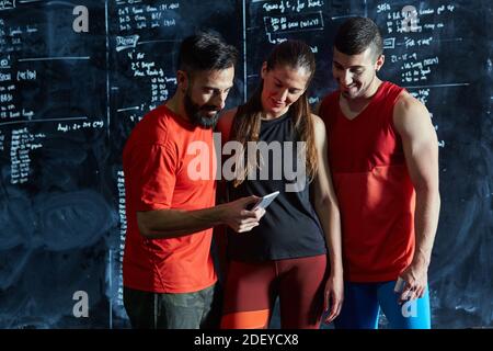 Stock photo from behind of tree people checking workout plans on a chalkboard. There are two males and a female. They are unrecognizable. Stock Photo