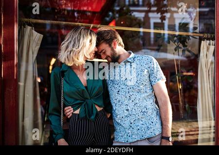 Stock photo of a couple in their 30s standing on the street. The man has his hands around the woman and his head on her shoulder. They are wearing cas Stock Photo