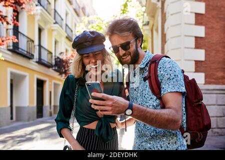 Stock photo of a couple in their 30s walking down a street and looking at a smartphone. They are wearing casual cloth. Stock Photo
