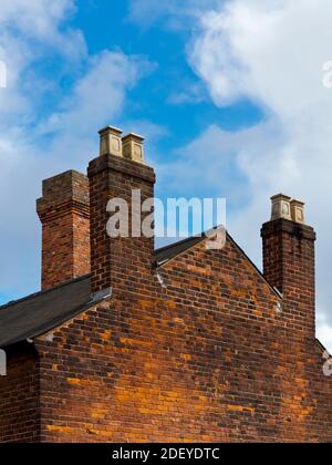 End wall of a red brick house with chimney pots and blue sky with clouds above. Stock Photo