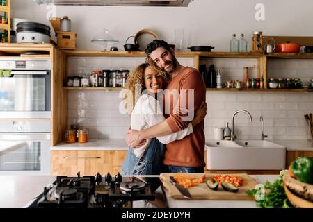 Stock photo of a middle aged woman and man standing in a kitchen and laughing. They are hugging. Stock Photo