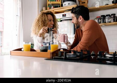 Stock photo of a middle aged woman and man having breakfast in a kitchen and laughing together. They are relaxed. Stock Photo