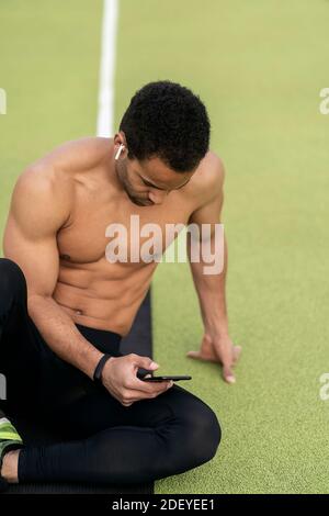 Stock photo of an afro athlete taking a break while using phone in sports track. Stock Photo
