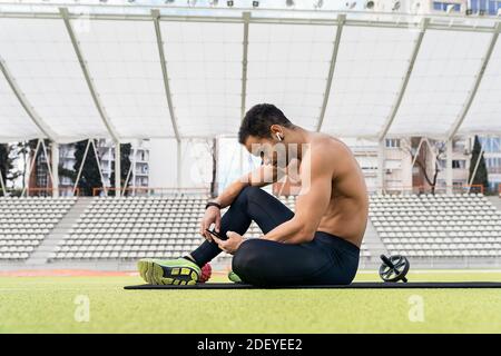 Stock photo of an afro athlete taking a break while using phone in sports track. Stock Photo
