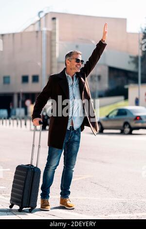 Stock photo of a caucasian business man calling a taxi in the airport. He is wearing casual clothes and sunglasses. He has a suitcase. Stock Photo
