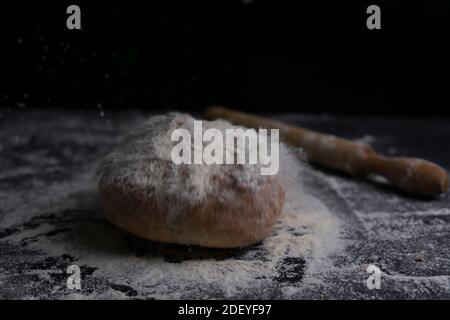 Fresh bread flying with flour splash and rolling pin on floury black table.Bakery and baking concept background.Copy Space. Stock Photo