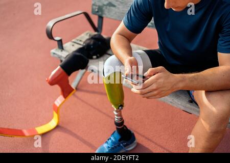 Disabled man athlete sitting in a bench using his phone in the stadium. Stock Photo