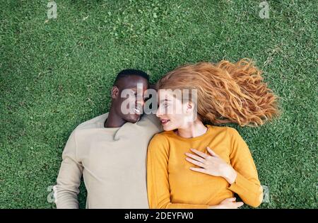 Stock photo of lovely young couple looking at each other while lying in the grass. Stock Photo