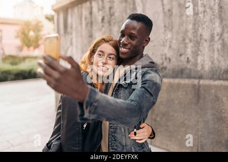 Stock photo of multiethnic couple taking selfie in the street. Stock Photo