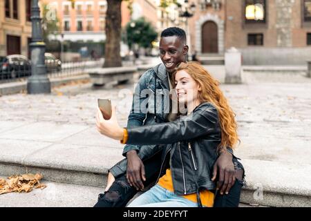 Stock photo of multiethnic couple taking selfie in the street. Stock Photo