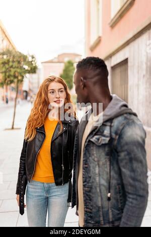 Stock photo of multiethnic young couple looking at each other while walking in the street. Stock Photo