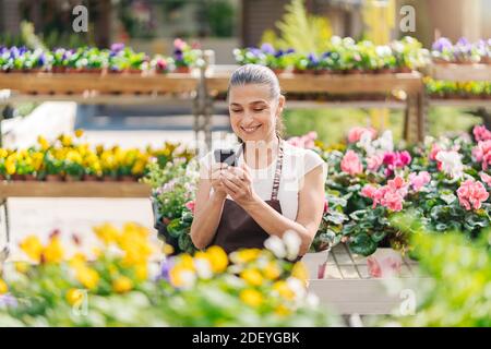 Stock photo of beautiful middle age woman working in plant nursery and using phone. Stock Photo