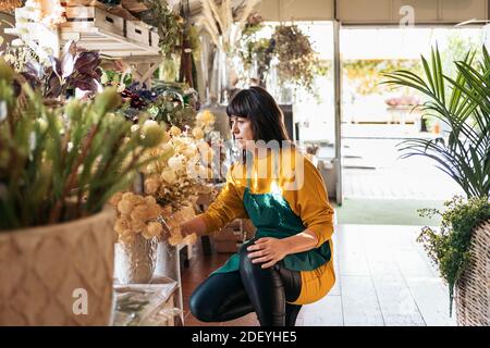 Stock photo of adult woman organizing flowers and plants in flower shop. Stock Photo