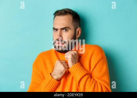 Close-up of scared bearded man looking startled and displeased, jumping from fear, standing over light blue background Stock Photo