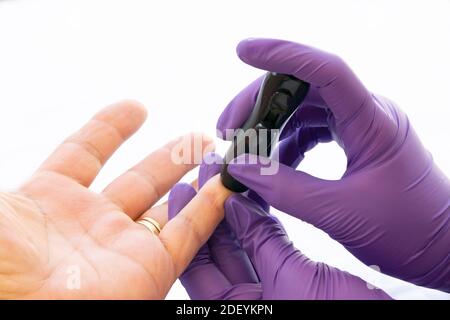 Close up of a healthcare assistant doing the glucose test to a diabetes patient on a white background. Stock Photo