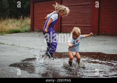 Brother and sister jumping in a big puddle having fun and laughing Stock Photo