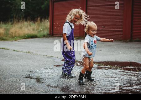 Siblings boy and girl jumping in a puddle having fun and smiling Stock Photo