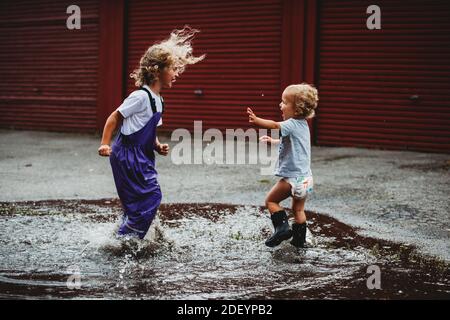 Siblings boy and girl jumping in a puddle having fun Stock Photo