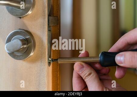 Carpenter repairing door lock. Installing a door handle. Handyman tightening door hinge . Hands of the repairman with a screwdriver. Locksmith screwin Stock Photo