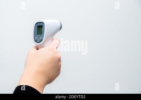 Doctor hand holding temperature gun on grey background. Close up of hand pointing thermometer in a hospital. Stock Photo