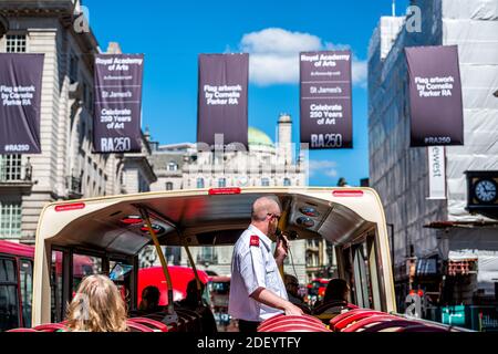 London, UK - June 22, 2018: Piccadilly street with many flags banners and point of view from red double decker big bus and tour guide Stock Photo