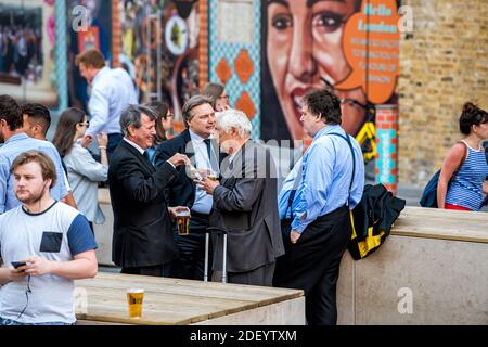 London, UK - June 22, 2018: Group of many businessmen people standing outside in England at the Shipwrights Arms pub tavern bar drinking beer from cup Stock Photo