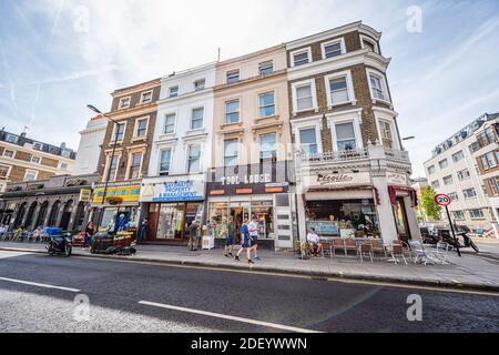 London, UK - June 24, 2018: Notting Hill Westbourne Grove street roads with people by hardware and bakery stores, sitting outside outdoor area at rest Stock Photo