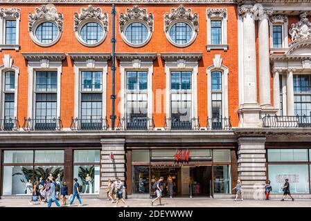 London, UK - June 24, 2018: Fitzrovia Terrace Victorian brick building on Oxford street road with sign for H&M store shop, people walking on sidewalk Stock Photo