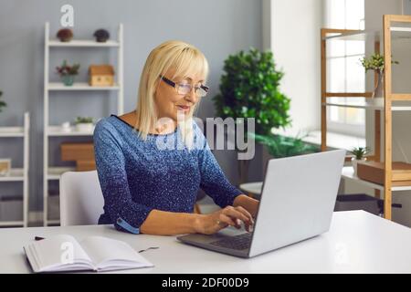 Inspired mature woman working on laptop, writing book or posting article on her blog Stock Photo