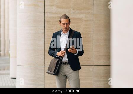 Young man in formal wear standing outdoors texting on cell phone Stock Photo