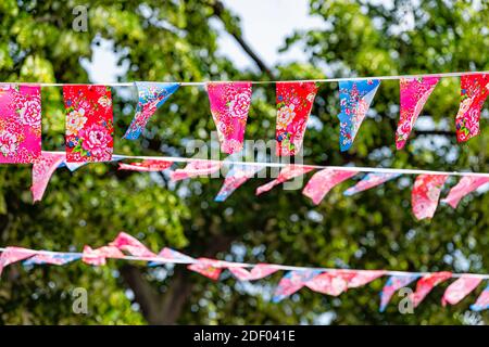 Rows of rope hanging banners flags in summer outdoors outside with colorful Asian rose flowers patterns in park at Chelsea area, London United Kingdom Stock Photo