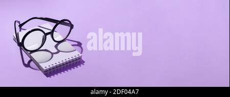 black round glasses lie on a Notepad and cast a shadow on the mint background Stock Photo