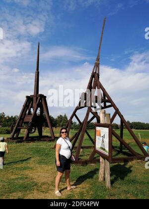 WENECJA, POLAND - Aug 20, 2020: Wooden old catapult with people on green grass by a outdoor museum. Stock Photo