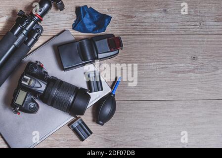 top view of a wooden table with photography equipment like digital professional camera, external flash unit, tripod, cleaning accessories and batterie Stock Photo
