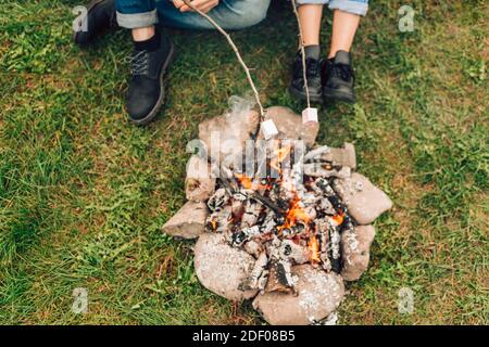 Legs of couple near fire who are roasting marshmallows. Picnic conceptLegs of couple near fire who are roasting marshmallows. Picnic concept Stock Photo