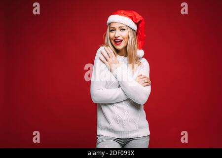 Cute woman in Santa hat embracing herself. Stock Photo