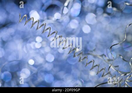 Detail of long spiral twisted aluminum swarf on blue background. Closeup of metal waste in turning. Chip machining by-product. Mechanical engineering. Stock Photo