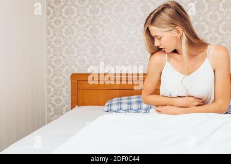 A young girl woke up in the morning and sitting in bed holding her stomach, Her face showing the pain she is getting. The concept of abdominal pain, s Stock Photo