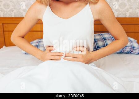 A young girl woke up in the morning and sitting in bed, holding her stomach, she feels severe abdominal pain, the Concept of abdominal pain, symptom, Stock Photo