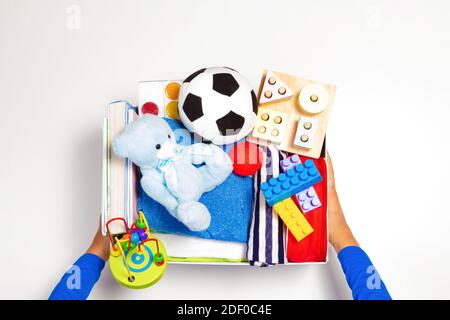 Donation concept. Volunteer hands holding donate box with clothes, books and toys on white background. Top view Stock Photo