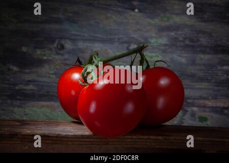 Macro Shot of Three Shinny Vivid Red Tomatoes on Table and Decayed Wooden Background Stock Photo
