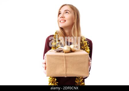 Pensive young woman, wearing a Santa Claus hat, dreams, looking to the side, in her hands, a gift box on a white background. Christmas Stock Photo