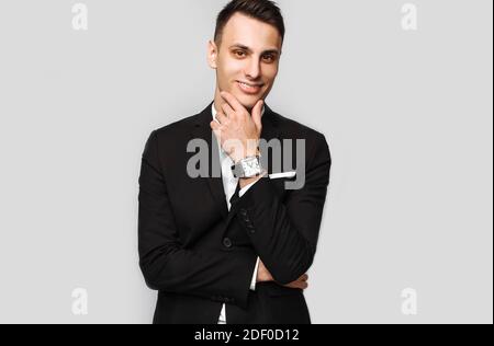Portrait of a handsome young business man, male, in a classic black suit, on a gray background. Business concept, career. Stock Photo