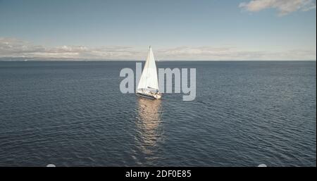 Alone sail yacht reflect at ocean water surface aerial. Racing sailboat at open sea. Luxury vessel at summer cruise. Cinematic soft sun light over wide serene seascape. Scenic marine shot
