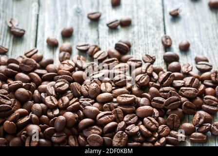 roasted coffee beans piled on bottom side of gray rustic wooden surface, backlit with natural light Stock Photo